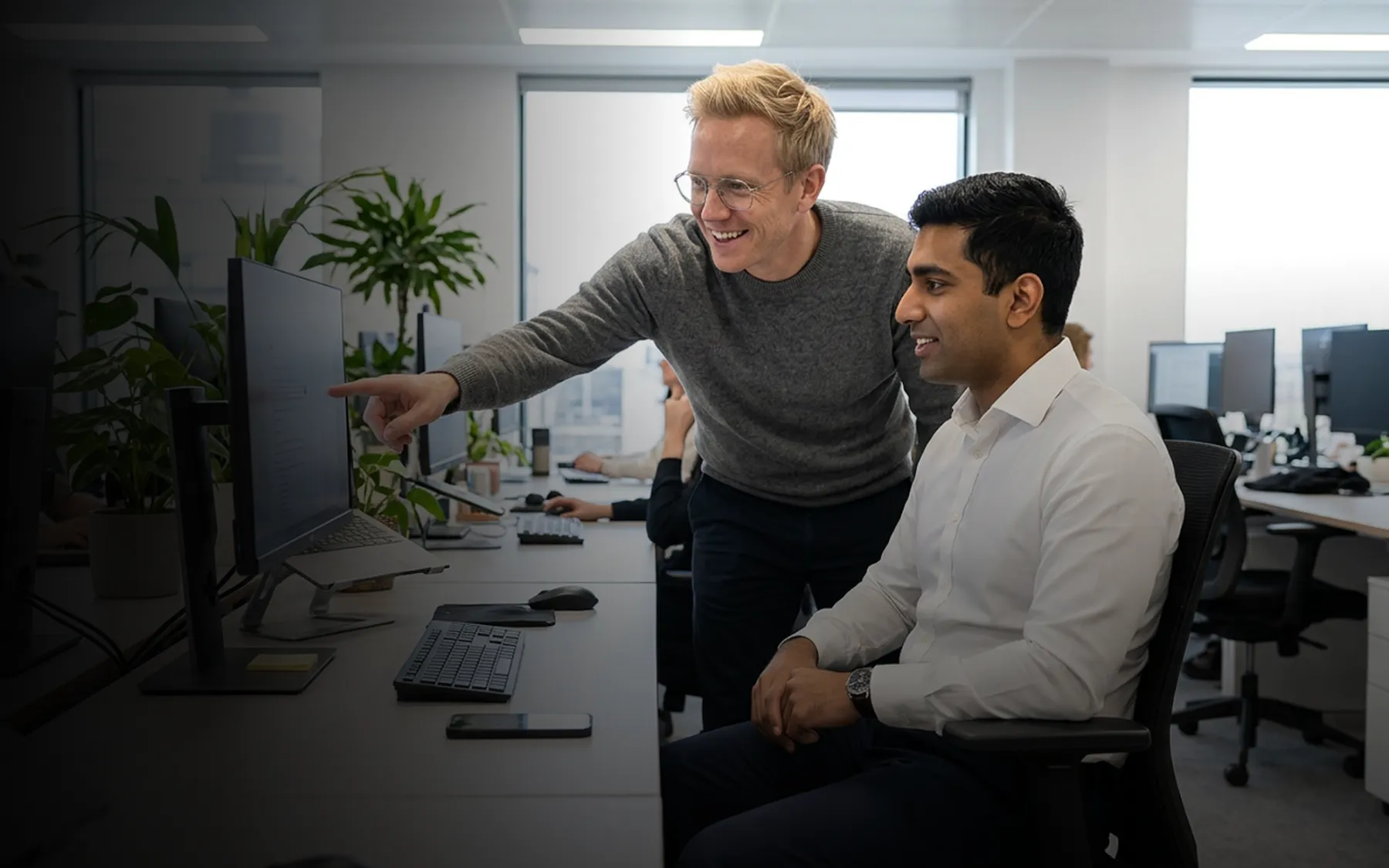 Two colleagues reviewing work at a shared workstation